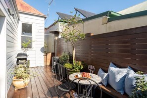 A patio with a table, chairs, a small garden, and a wooden fence. - Charming Leichhardt Cottage with BBQ Deck (Leichhardt)