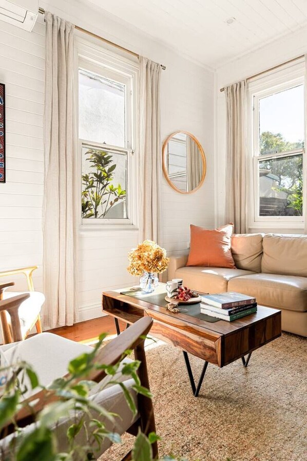 A living room with a sofa, coffee table, and a mirror. - Charming Leichhardt Cottage with BBQ Deck (Leichhardt)