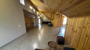 Un hall d’entrée spacieux aux murs en bois et au plafond haut, comprenant un coin salon avec une table ronde et des bancs.