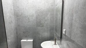 Une salle de bain avec des toilettes et un lavabo, tous deux de couleur blanche, devant un mur recouvert de carreaux gris.