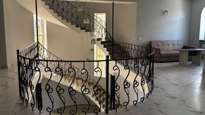 Un vaste espace de vie doté d’un sol en marbre, d’un escalier circulaire en métal noir agrémenté de rampes décoratives, d’un canapé et d’une table.
