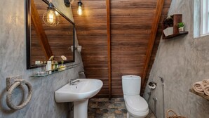 Ein Badezimmer mit Steinfliesen, einem weißen Waschbecken, einer Toilette und einer Holzkollektion.