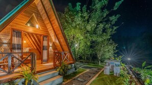 Eine Holzhütte mit einem Giebeldach, einer Veranda mit Geländer und einem Garten mit einem Kiesweg.