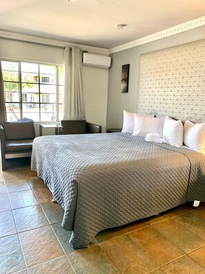 Habitación de hotel con una cama grande, una mesita, una silla y una ventana con cortinas.