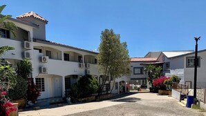 Un edificio de varios pisos con balcones, un patio interior y abundante vegetación alrededor.