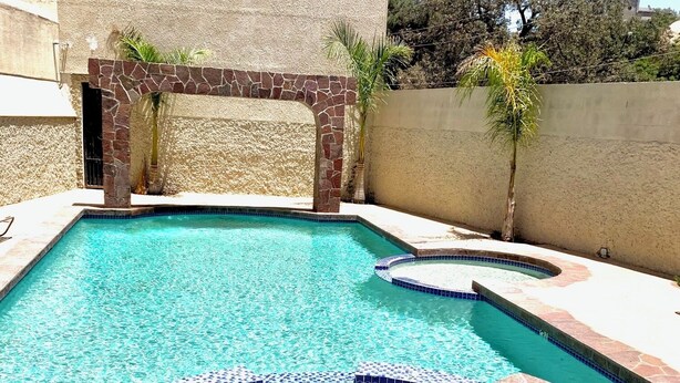 Una piscina con un arco de piedra, un jacuzzi y un borde de piedra.