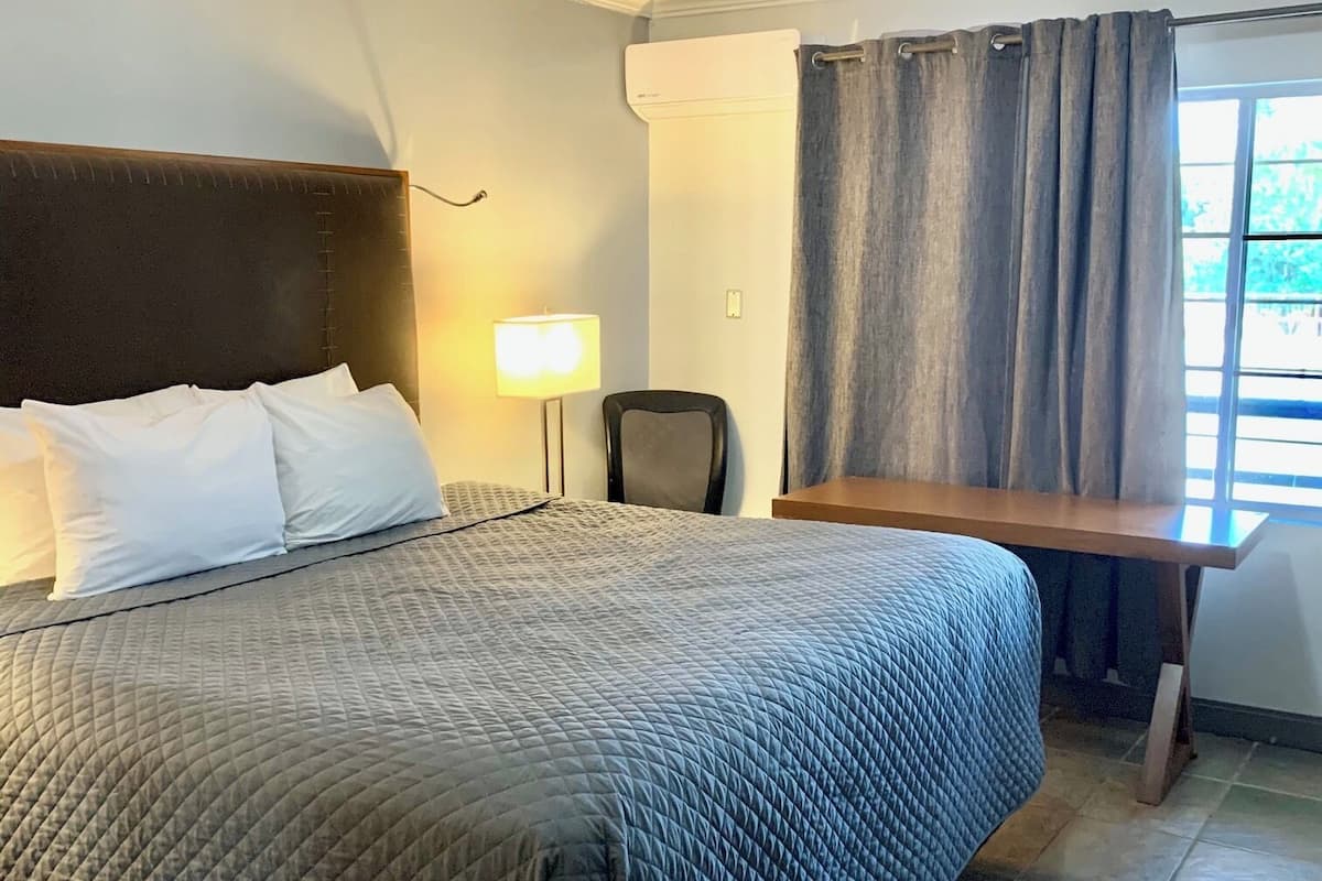 Ein Hotelzimmer mit Bett, Schreibtisch, Lampe und einem fensterbepflanzten Fenster.