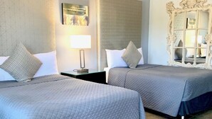 Habitación de hotel con dos camas, una mesita de noche con lámpara, un espejo decorativo y un cuadro en la pared.