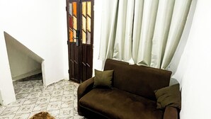A living room with a brown sofa, a patterned rug, a door with stained glass, and a white curtain.