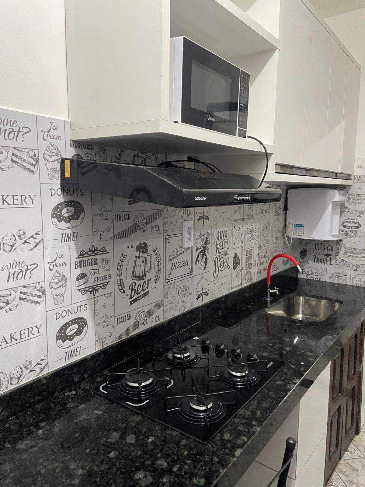 A kitchen with a black countertop, stainless steel sink, and a gas stove.