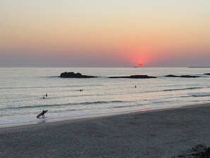 A beach scene with a sunset, calm sea, and a few people.