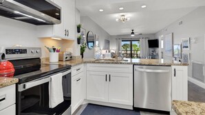 Una cocina moderna con armarios blancos, electrodomésticos de acero inoxidable, encimera de granito y vistas al exterior.