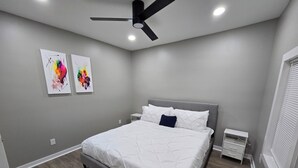 Ein Schlafzimmer mit einem Bett, einem Deckenventilator, zwei Wandbildern und einem Nachttisch.