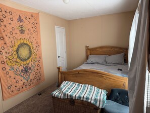 Una camera da letto con un letto, una testiera in legno, un cesto di vimini e un arazzo con motivi floreali.