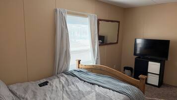 A hotel room with a bed, a television, a mirror, and a window with curtains.