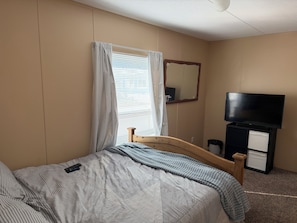 Una camera d'albergo con un letto, una televisione, uno specchio e una finestra con tende.