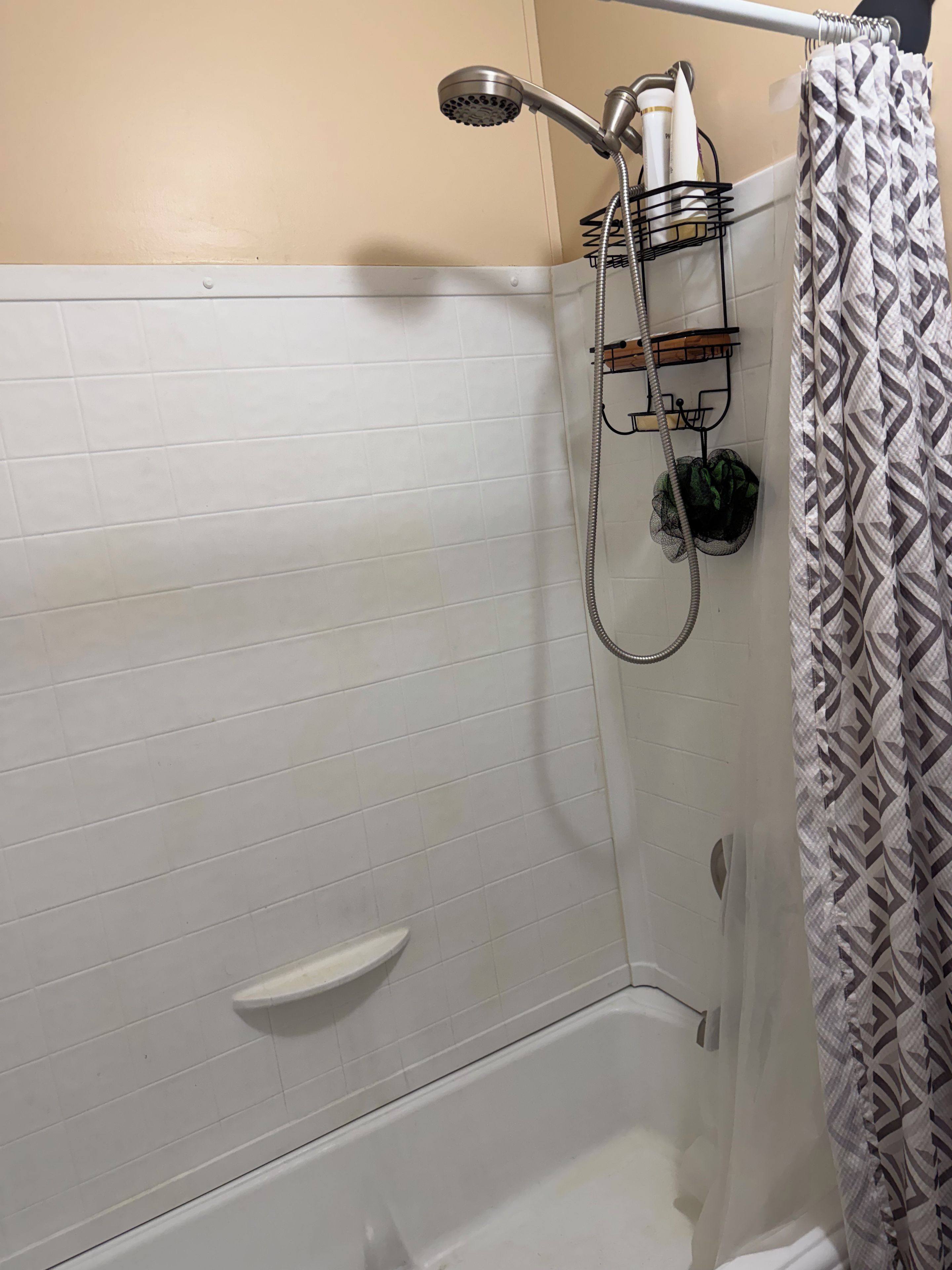 A shower area with a handheld showerhead, a towel rack with a towel, and a shower caddy.