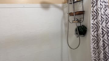 A shower area with a handheld showerhead, a towel rack with a towel, and a shower caddy.