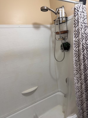 A shower area with a handheld showerhead, a towel rack with a towel, and a shower caddy.