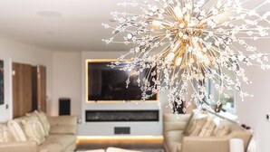Un salon moderne avec un grand téléviseur, un lustre décoratif et un canapé.