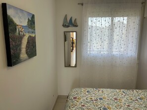 Ein Schlafzimmer mit einem Bett, einem Gemälde, einem Spiegel und einem Fenster mit floralem Vorhang.