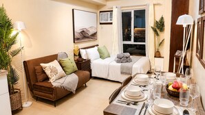 A compact living space with a sofa, a dining table set for four, and a bed with a view of the city at night. - Cozy 29F Avida Riala IT Park Sea & City View (Cebu City)
