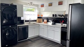 A modern kitchen with white cabinets, a black refrigerator, a built-in washing machine, and a coffee maker. - Sunny townhome:walk to UD & stadium (Newark)
