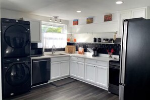Una cocina moderna con armarios blancos, un refrigerador negro, lavadora integrada y una cafetera.