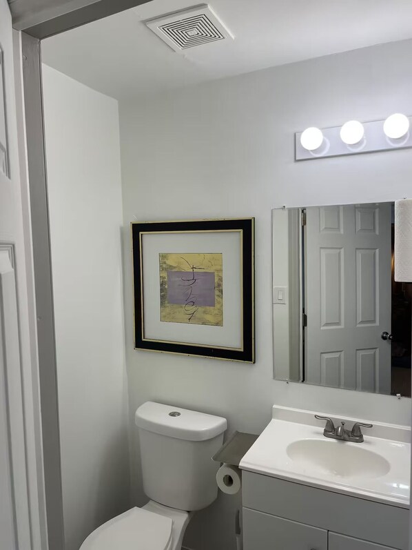 Un baño con inodoro, lavamanos, una obra de arte enmarcada y un espejo con iluminación.