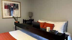 A hotel room with a bed, a desk with a laptop, a plant, a lamp, and a framed picture on the wall. - Sunny townhome:walk to UD & stadium (Newark)