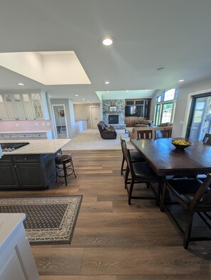 A spacious kitchen with a central island, a dining area with a wooden table, and a stone fireplace. - New! Spacious 4-bedroom house in Traverse City just minutes from the beach! (Traverse City)