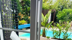 Une porte vitrée donne accès à un espace aménagé au bord de la piscine, avec un fauteuil de relaxation et une serviette.
