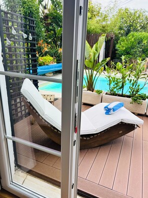 Eine Glastür führt zu einem Poolbereich mit Liege und Handtuch.
