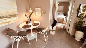 Un coin repas comprenant une table ronde, des chaises, un vase avec des fleurs, un tableau encadré et une lampe fixée au mur.