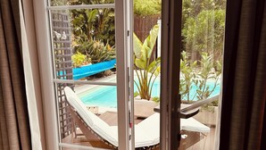 Une pièce dotée d’une porte-fenêtre coulissante donnant sur un espace extérieur avec une piscine, des chaises longues et des plantes tropicales.