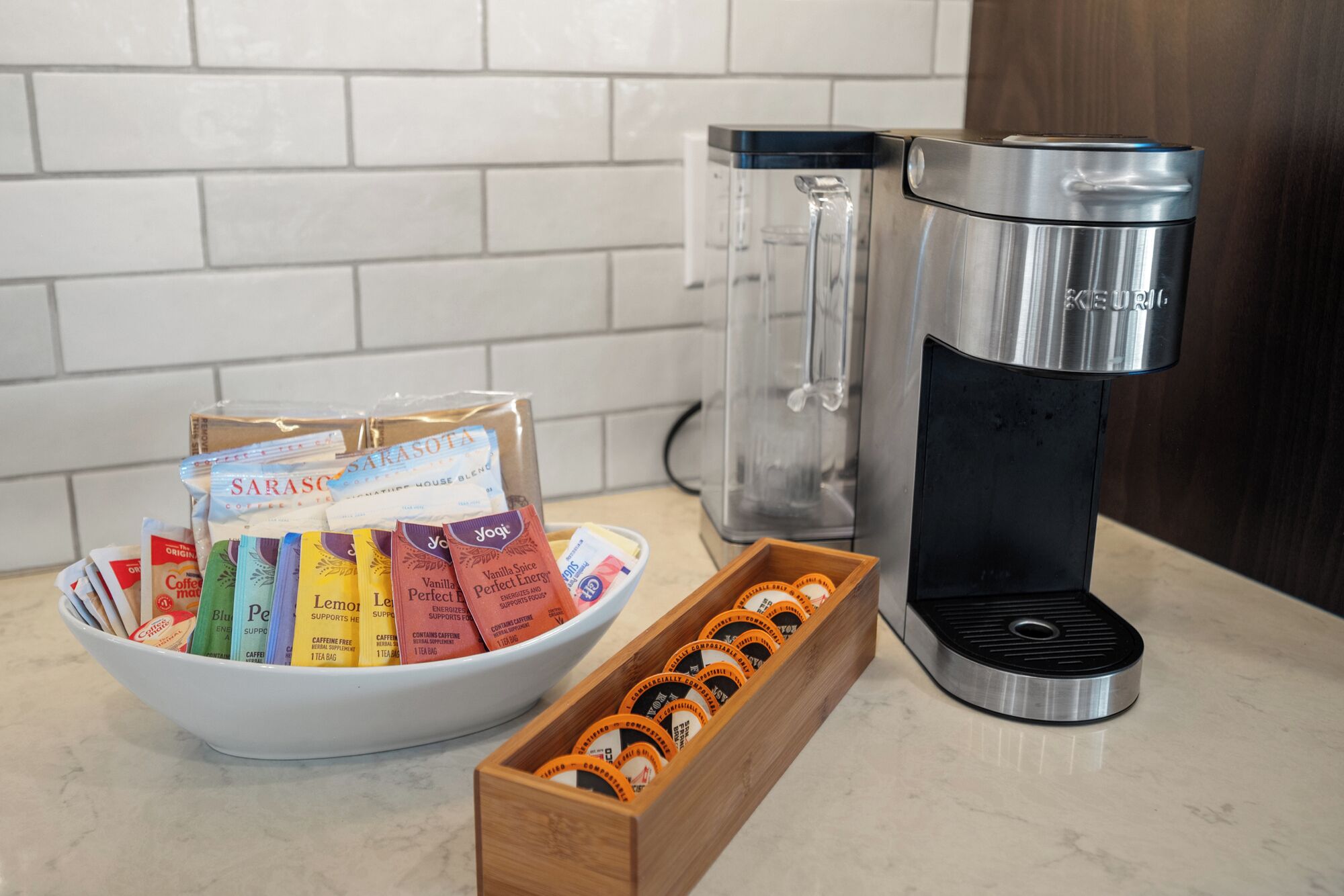 A coffee maker, a bowl of coffee pods, and a box of coffee capsules on a kitchen counter.