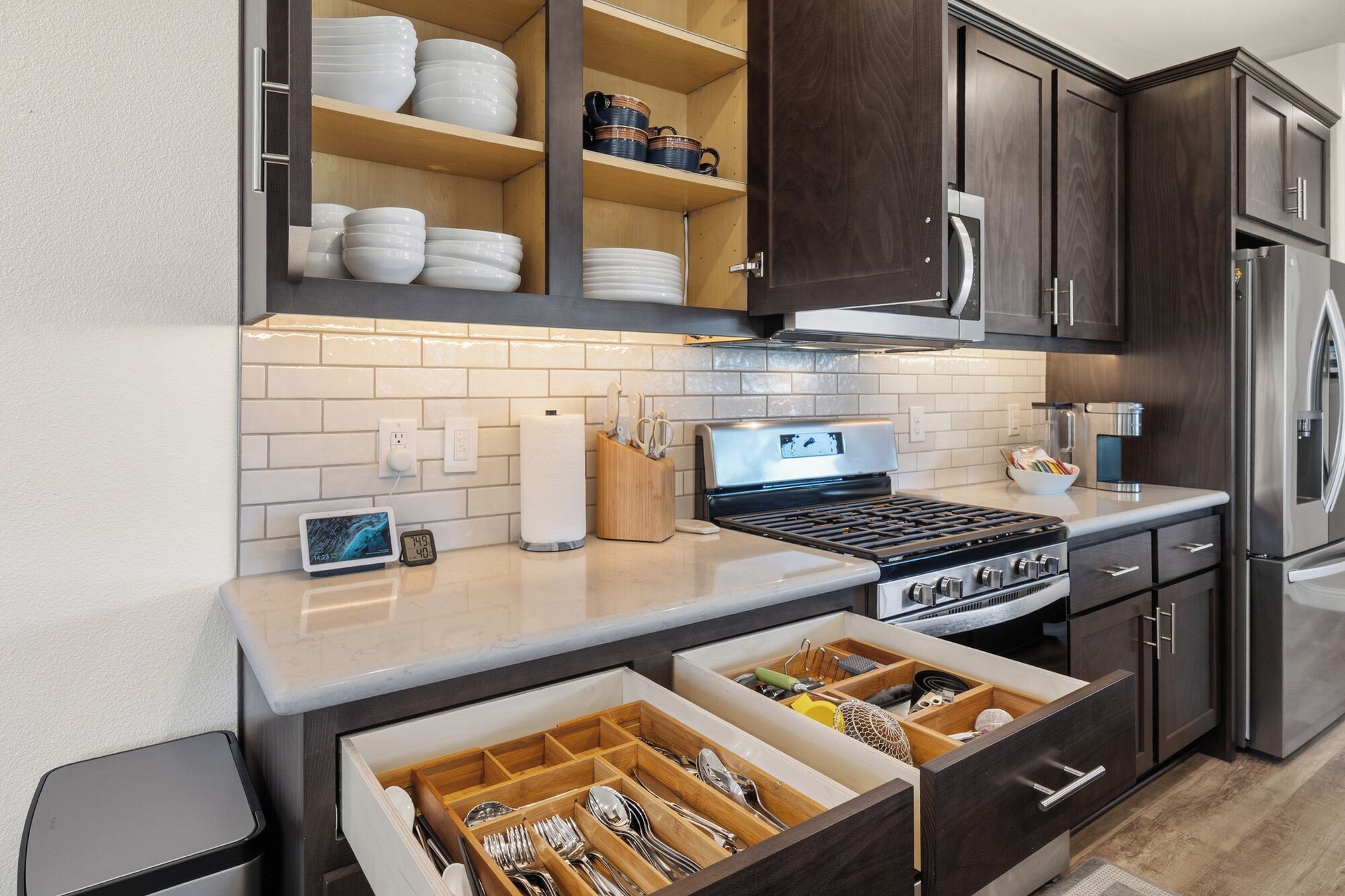 Una cocina moderna con armarios de madera oscura, un refrigerador de acero inoxidable, un horno empotrado y una encimera con una tableta y un reloj.