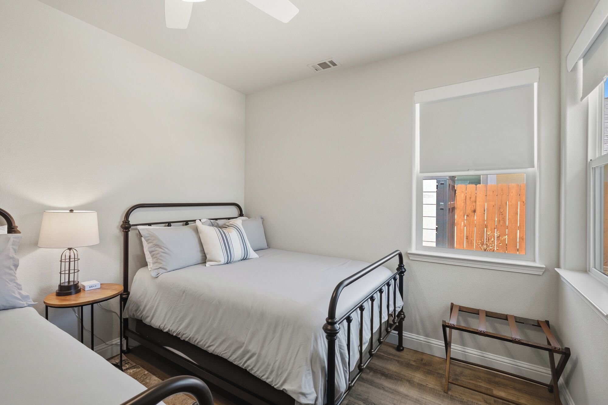 Un dormitorio con cama, mesita de noche, lámpara, ventana y un taburete de madera.