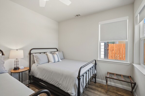 A bedroom with a bed, bedside table, lamp, window, and a small wooden stool.