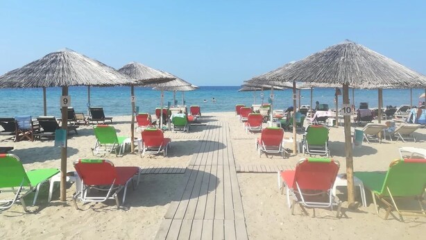 Une plage bordée de rangées de chaises longues et d’ombrelles en chaume, une promenade en bois et l’océan en toile de fond.