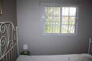 Ein Schlafzimmer mit einem Einzelbett, einem Fenster mit Gartenblick und einem Nachttisch mit Lampe.