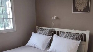 Un lit bien fait, avec une tête de lit blanche, une fenêtre avec des stores et un luminaire fixé au mur.