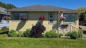 A two-story house with a stone foundation, a yellow exterior, and hanging flower baskets.