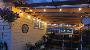 A covered outdoor area with exercise equipment, seating, and hanging flower baskets.