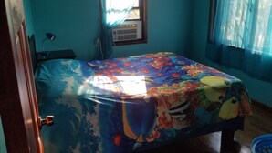 Un dormitorio con cama, ventana con cortinas, aire acondicionado y escritorio con lámpara.