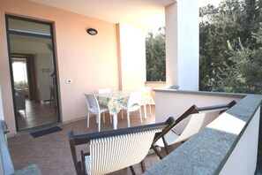 Ein Balkon mit Tisch und Stühlen, eine Tür zum Innenbereich und Blick auf Bäume.