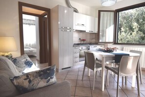 Eine moderne Küche mit weißen Schränken, einem Esstisch mit Stühlen und Blick durch ein Fenster.
