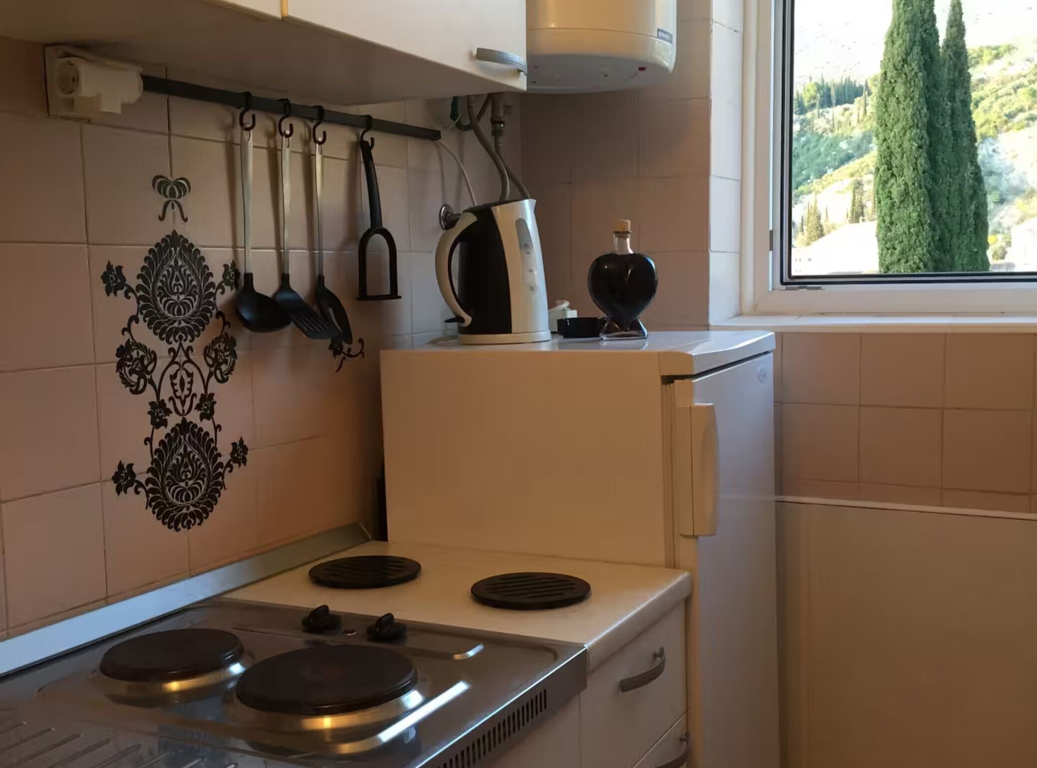 Eine Küche mit Herd, hängenden Töpfen und einem Fenster mit Blick auf Bäume.
