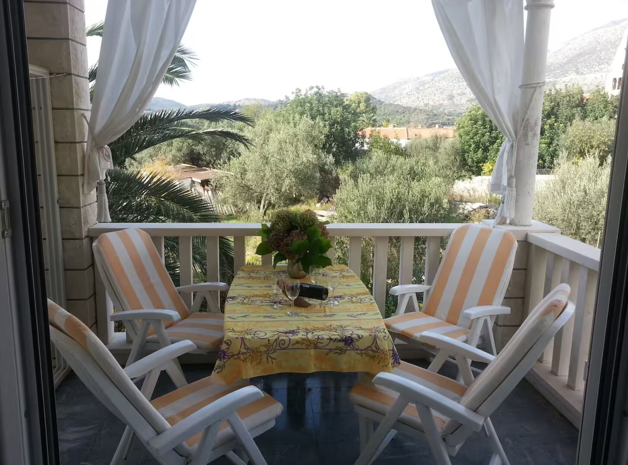 A balcony with a table, chairs, and a view of a mountainous landscape.