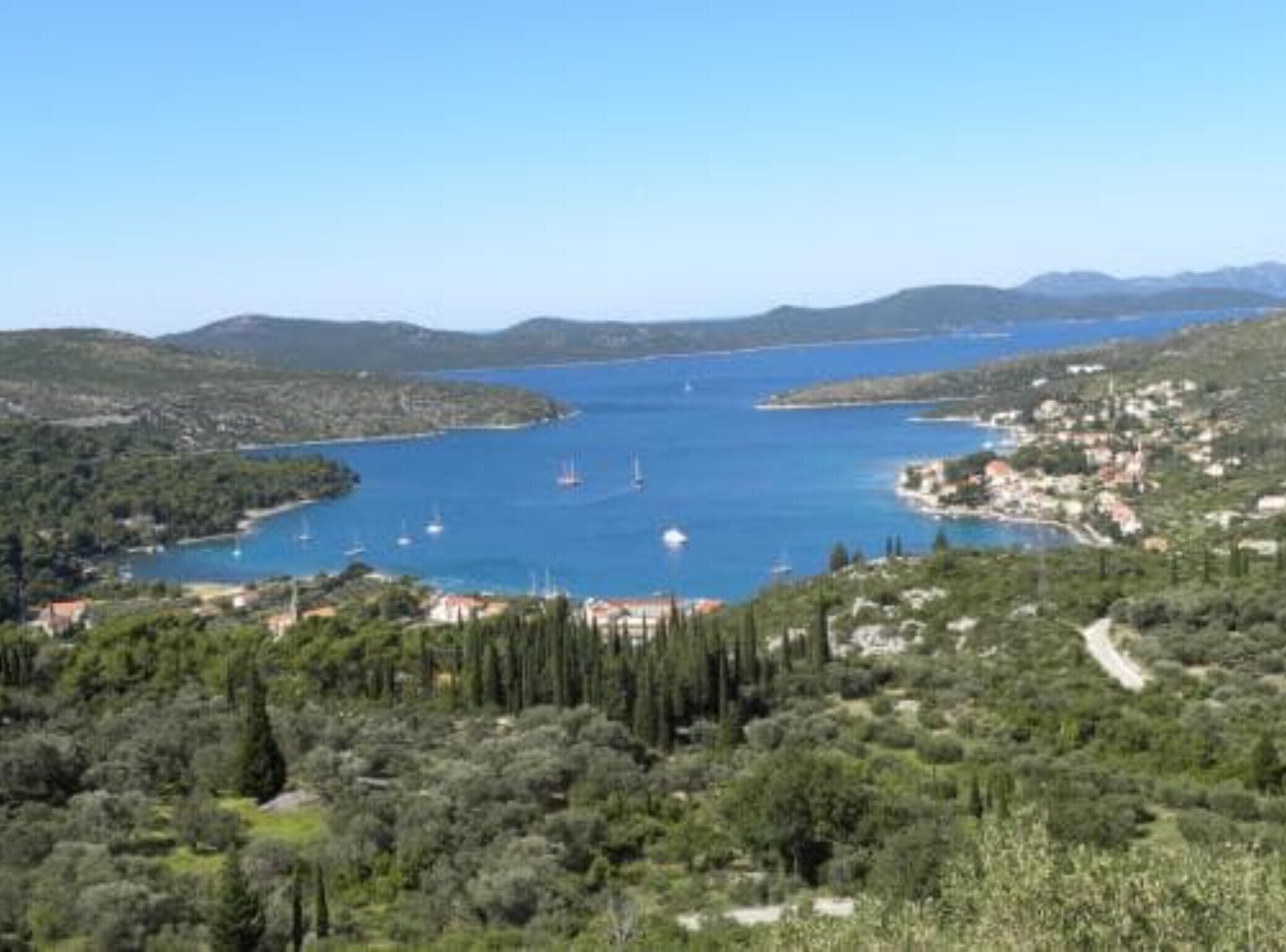 Paisaje costero con vista despejada a una bahía, barcos y un pueblo con edificios y vegetación.